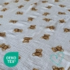 Zbliżenie na pofalowaną fakturę muślinu bawełnianego Double Gauze we wzór w klasyczne brązowe misie na śmietankowym tle. W lewym dolnym rogu widoczne jest zielone logo certyfikatu OEKO-TEX®, potwierdzające bezpieczeństwo tkaniny