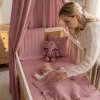 Prześcieradło z gumką 120x60 brudny róż w zestawie wyprawkowym. Bawełniane prześcieradło do łóżeczka, kolor antyczny róż, pokazane w przytulnej aranżacji z mamą, śpiącym dzieckiem i baldachimem.