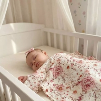 Śpiące niemowlę w łóżeczku przykryte lekkim kocykiem w kwiatowy wzór róż i koronki