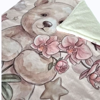 Zbliżenie na misia Lilu z różową orchideą na kocyku Minky i odwinięty kremowy róg.