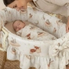 Mama patrząca na śpiące niemowlę w koszu z ochraniaczem w stylu boho.