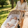 Uśmiechnięta mama spacerująca z wózkiem, widoczne prześcieradło ze zwierzątkami wewnątrz gondoli.