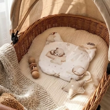 Płaska poduszka niemowlęca w kształcie misia z motywem zwierząt leśnych leżąca w wiklinowym koszu Mojżesza.
