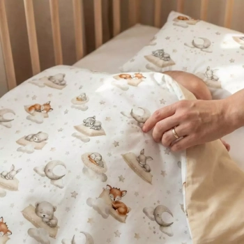 Ręka dorosłej osoby poprawiająca dwustronną kołdrę niemowlęcą (wzór leśne zwierzęta) śpiącemu dziecku.