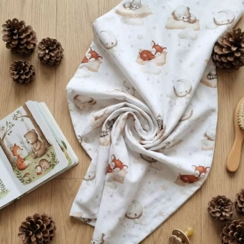 Artystyczna kompozycja: bawełniane prześcieradło okrągłe Mu&Mu w otoczeniu szyszek, książeczki dla dzieci i akcesoriów z drewna. Stylistyka Scandi i Boho.