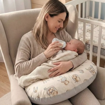 Mama karmiąca butelką noworodka przy użyciu beżowej poduszki do karmienia odciążającej kręgosłup.