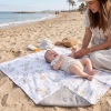 Dwustronny kocyk niemowlęcy (bawełna/muślin) rozłożony na plaży. Niemowlę leżące na bawełnianej stronie we wzór Kołysanka z Safari, widoczny jasnoszary spód.
