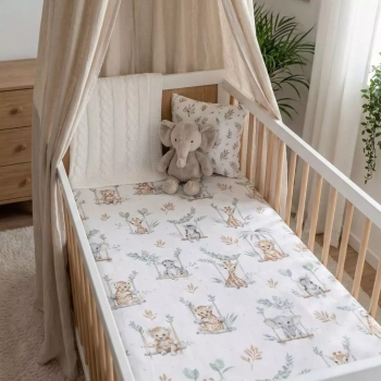 uste łóżeczko niemowlęce z baldachimem i prześcieradłem w wzór Safari. W rogu łóżeczka siedzi pluszowy słonik. Jasna, przytulna aranżacja.