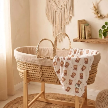 Przytulna aranżacja pokoju dziecięcego w stylu boho. Przewiewny kocyk niemowlęcy z bawełny ażurowej we wzór 'Misiowa Kraina' (brązowe misie w mięciutkich kapturkach z uszkami) swobodnie przewieszony przez krawędź plecionego kosza Mojżesza na drewnianym st