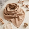 Artystyczne ujęcie typu flat lay chusty muślinowej w karmelowym odcieniu, zwiniętej centralnie w spiralę. Na jasnym, lni
