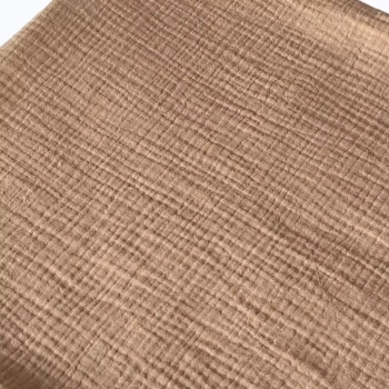Detaliczne zbliżenie na naturalną, pofalowaną fakturę muślinu bawełnianego w eleganckim odcieniu ciemnego beżu (Coffee), ukazujące charakterystyczny, oddychający splot tkaniny.