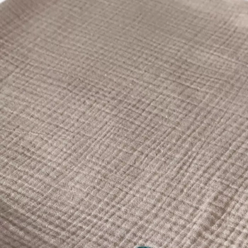 Zbliżenie na fakturę letniego kocyka muślinowego dla niemowlaka w kolorze jasnego beżu. Wyraźnie widoczna naturalna, karbowana struktura tkaniny Double Gauze.