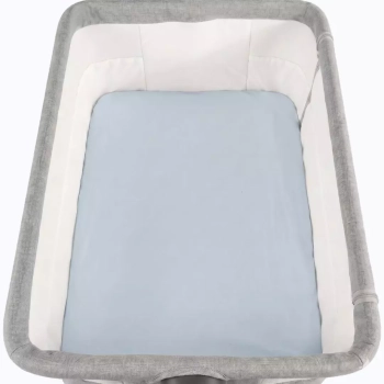 Widok z góry na jasnoniebieskie prześcieradło z gumką, założone na materac w szarym łóżeczku dostawnym. Packshot na białym tle pokazuje gładką strukturę błękitnej bawełny oraz estetyczne dopasowanie materiału do prostokątnego wnętrza dostawki.
