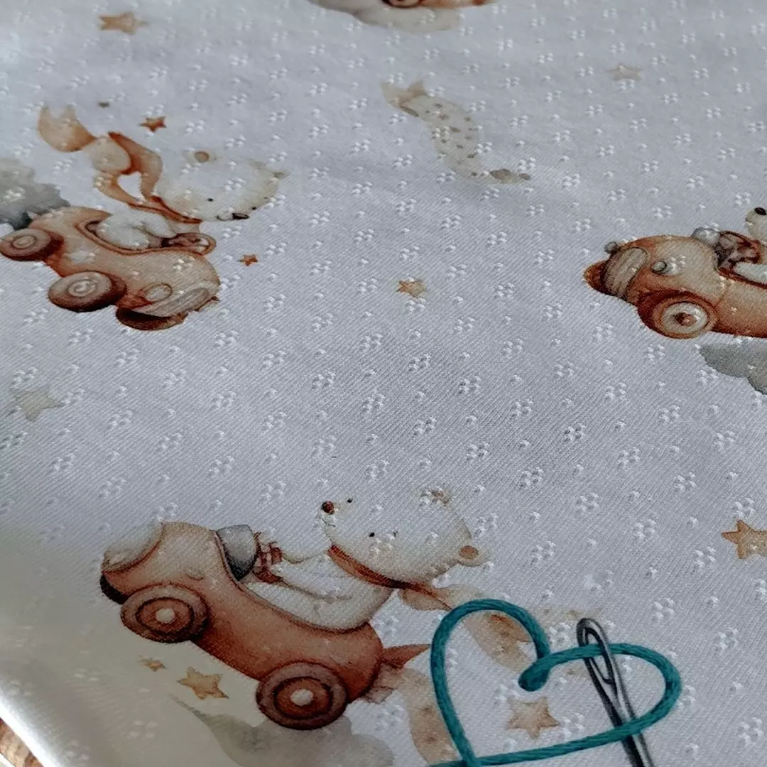Letni kocyk niemowlęcy z przewiewnej bawełny ażurowej we wzór Podniebny Rajd - urocze misie w karmelowych autkach retro jadące po chmurkach. Widoczna struktura oddychającej dzianiny pointelle.