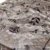 Zbliżenie na bawełnianą tkaninę pościeli niemowlęcej. Botaniczny wzór Retro Bloom z akwarelowymi piwoniami w kolorze brudnego różu i drobnymi polnymi kwiatami na szarobeżowym tle (taupe).