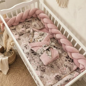 Kwiatowa kołderka niemowlęca z kolekcji Retro Bloom, na której leży tradycyjnie wiązany rożek w otoczeniu brudno-różowego ochraniacza warkocza.