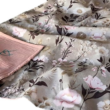Zbliżenie na miękko ułożony, dwustronny letni kocyk niemowlęcy we wzór Retro Bloom. Szarobeżowa bawełna w botaniczny motyw z piwoniami i ciemnymi liśćmi oraz odwinięty róg z karbowanego muślinu w kolorze brudnego różu.