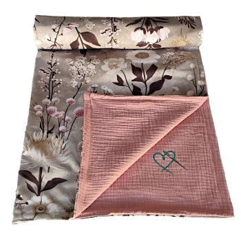 Częściowo zwinięty dwustronny kocyk niemowlęcy z bawełny i muślinu. Wyeksponowany kwiatowy wzór Retro Bloom na szarobeżowym tle oraz odchylony róg ukazujący karbowany spód w kolorze brudnego różu.