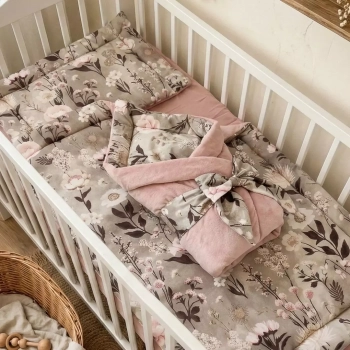 Zestaw pościeli niemowlęcej Retro Bloom. Na botanicznej kołderce z płaską poduszką leży tradycyjnie wiązany rożek w kwiaty.